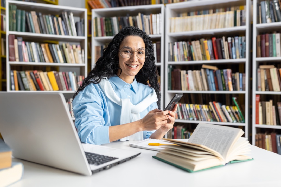 Woman smiling while working on a computer in a library