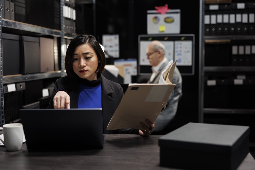 Woman in suit researching with a stack of archive folders