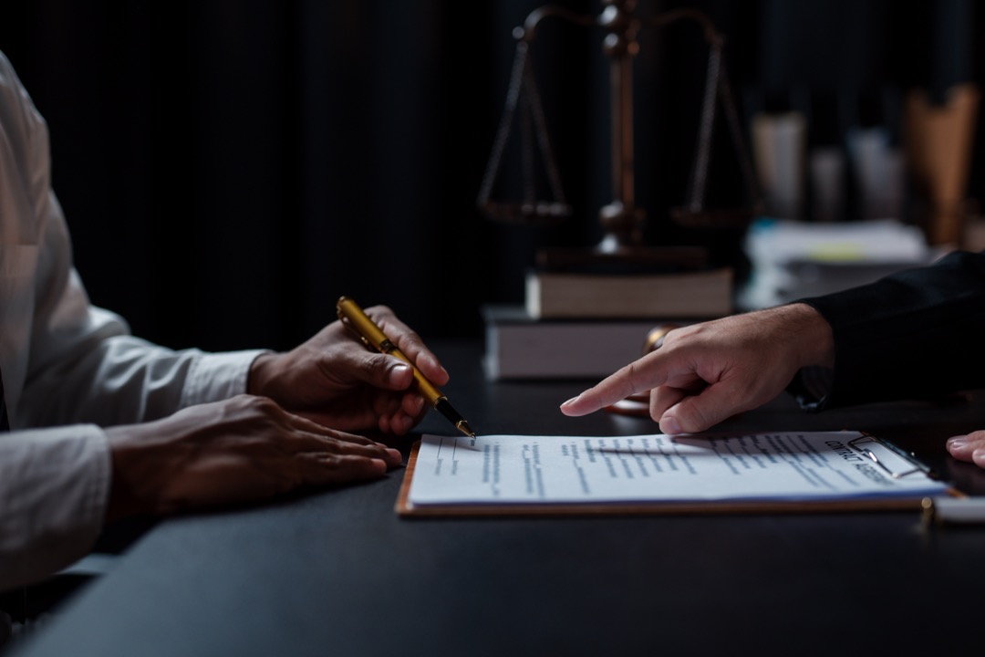 A person writing a legal document and the other person pointing to the document