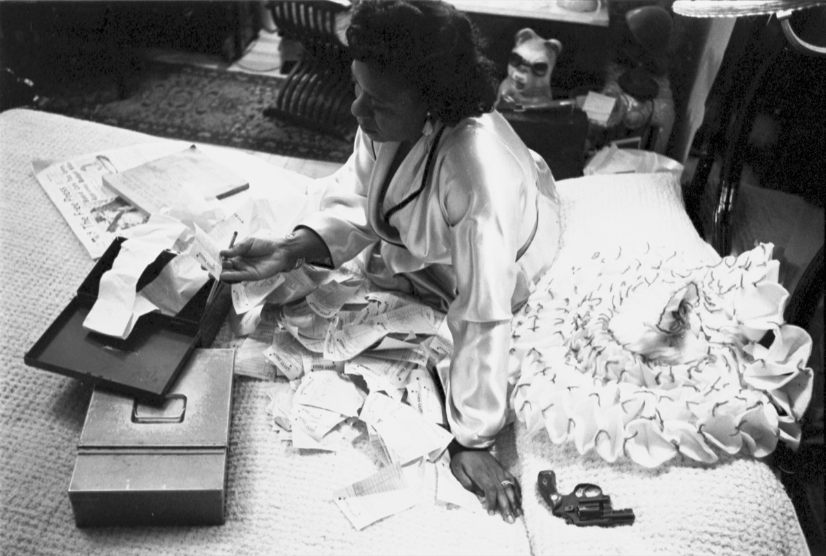 A black and white photo of an african american woman sitting on the bed going through photos
