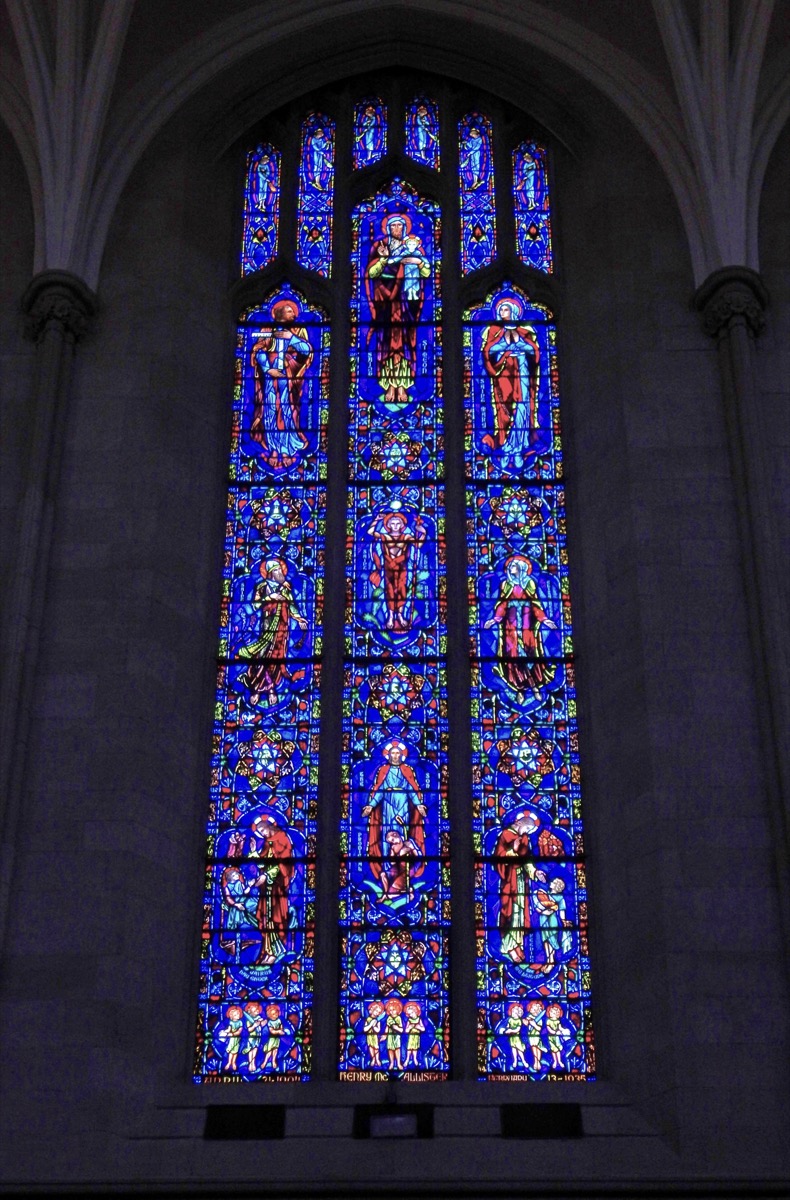 A photo of a large narrow blue stain glass window depicting a biblical scene