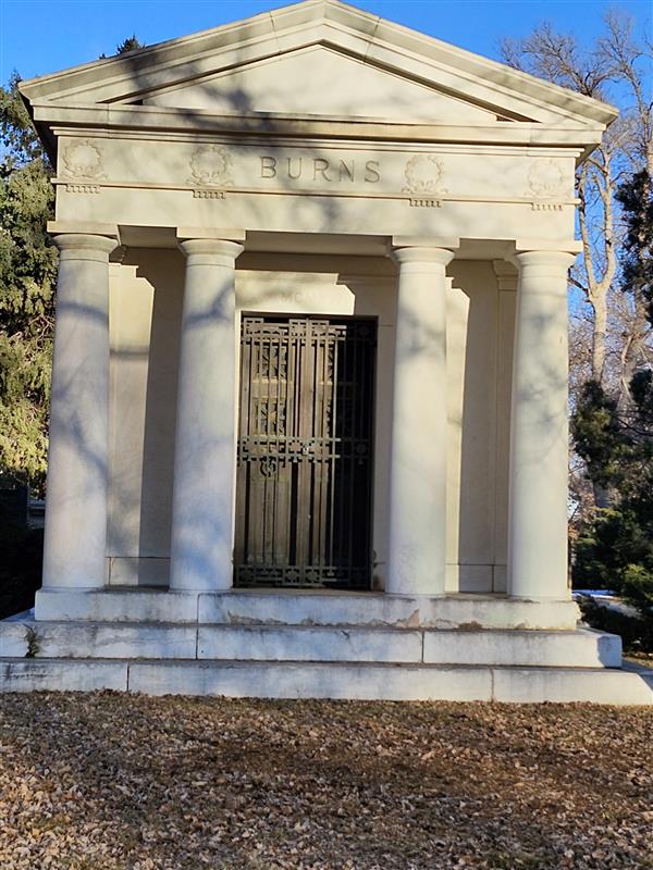 The front of a mausoleums showing 4 big roman style columns with a door in the middle