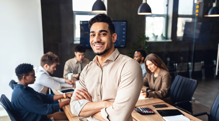 A person leaning on a desk posing with a group of business people working behind him