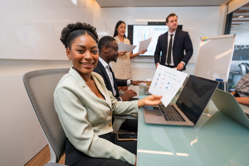 A professional business woman holding a piece of paper at a desk and a computer
