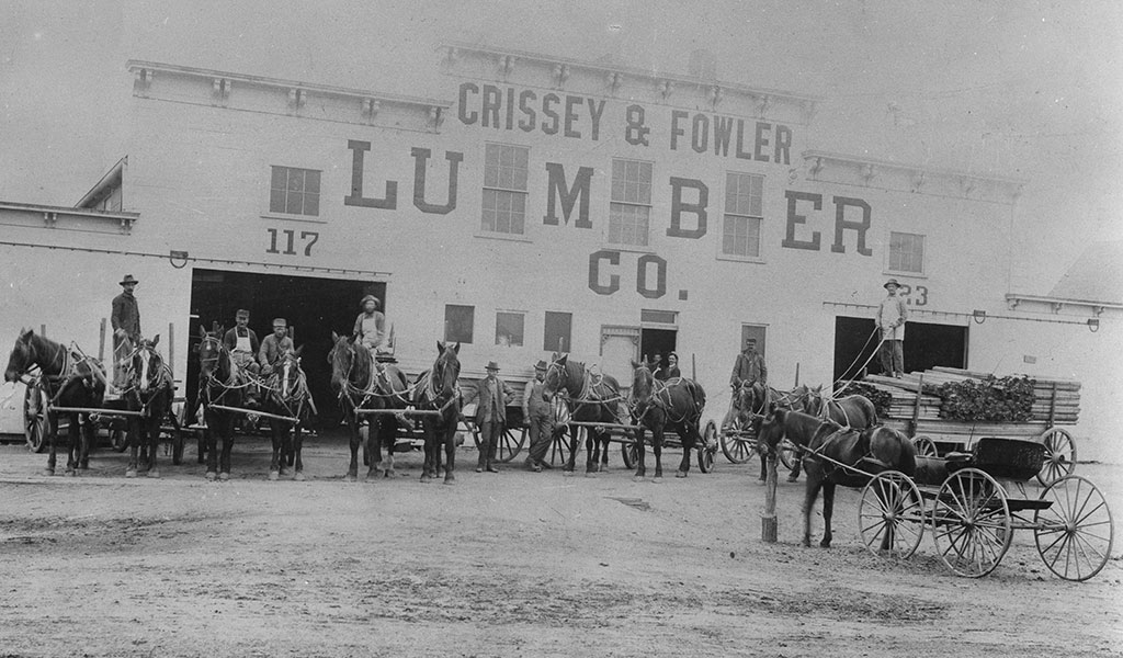 a black and white photo of Crissey & Fowler Lumber building with horses and wagons outside