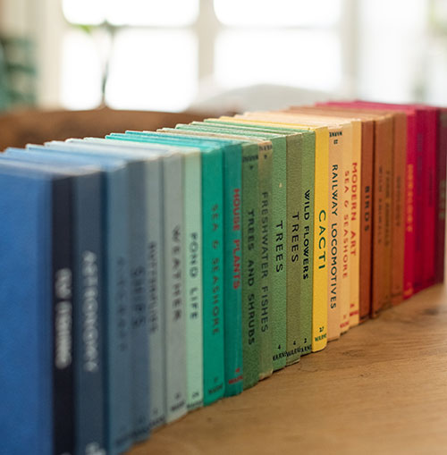 A set of rainbow colored books sitting up on a table