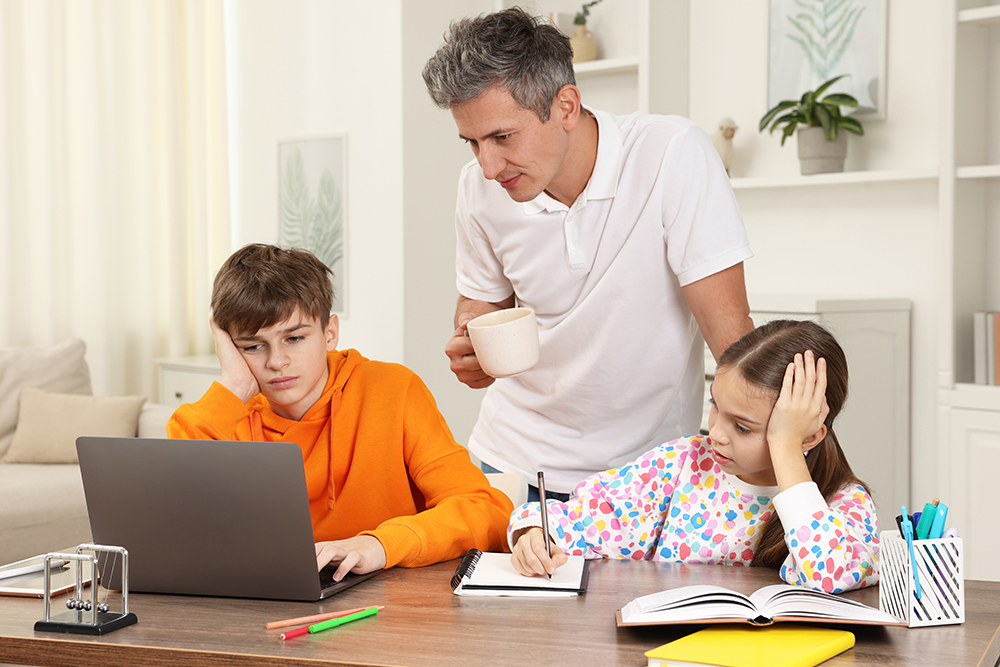 father helping his children with homework at a table