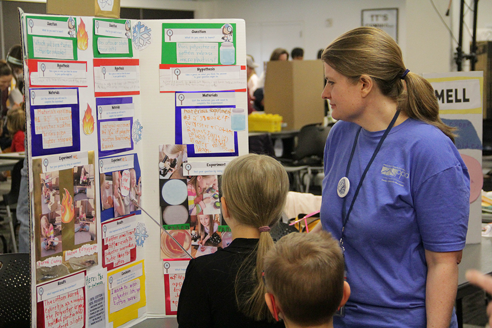Library employee looks at homeschool science fair entry with two students