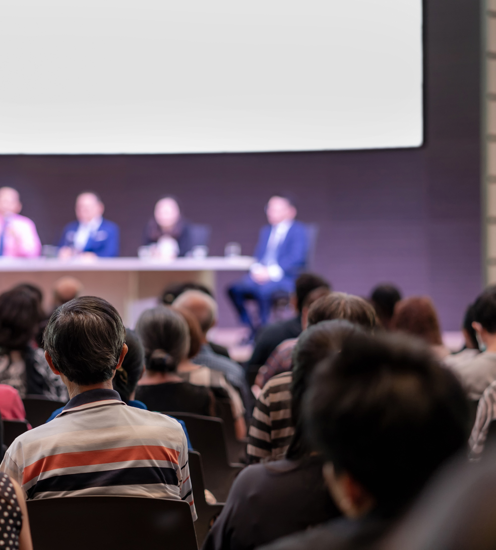 A photo of a crowd listening to a townhall meeting. The Room is very packed with lots of people in attendance.