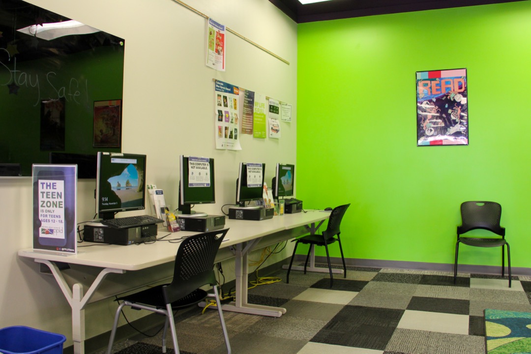 A line of Computers against the wall next to a black white board. This is the Teen Game Center in Ruth Holley Library