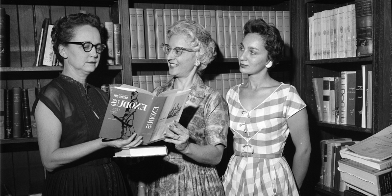 Historic photo of women in a library setting looking at a book together