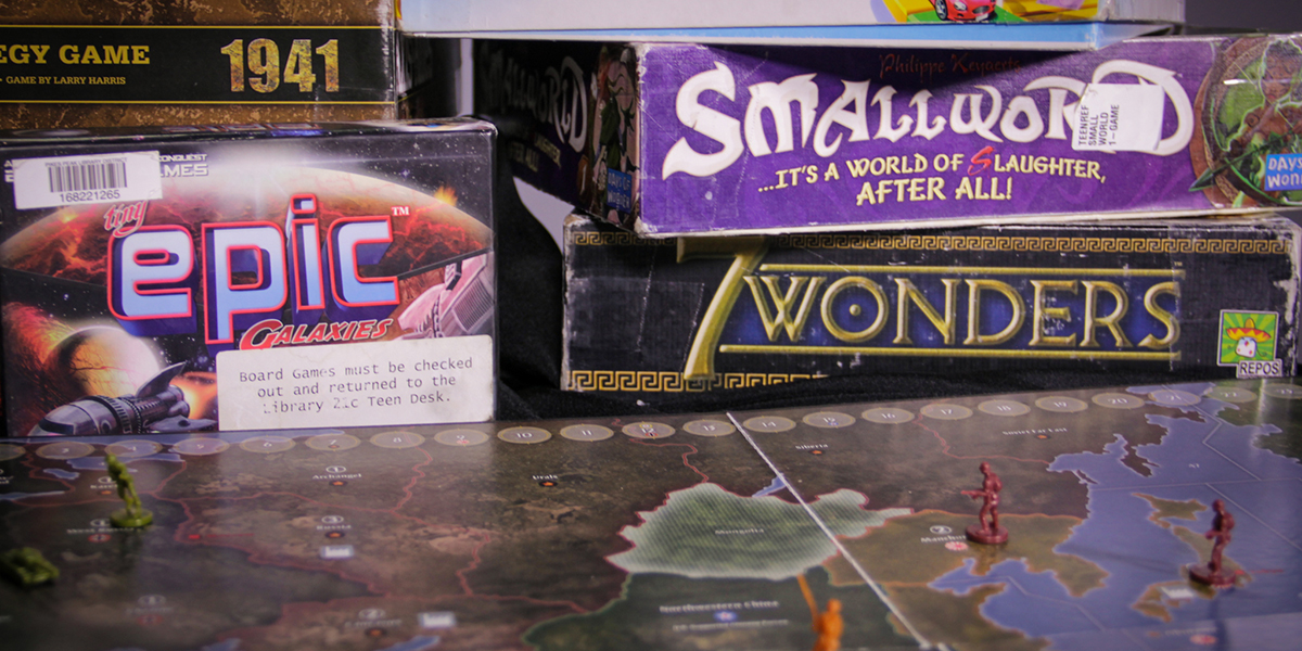 A board game’s map-printed board is open in front of several games still in their boxes.
