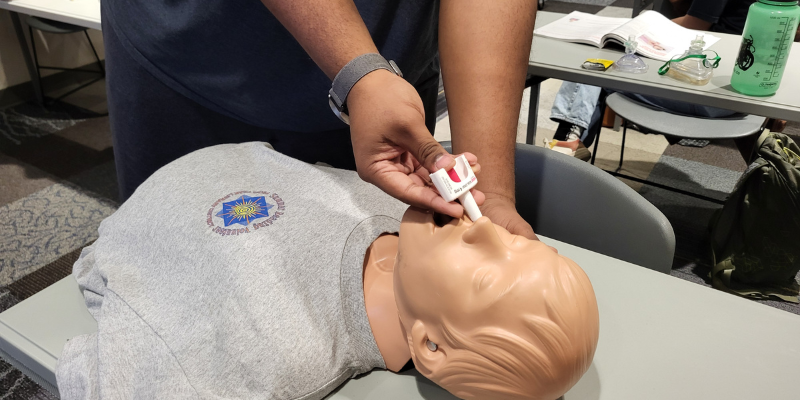 A trainee administers a tube of Narcan to a medical mannequin.  