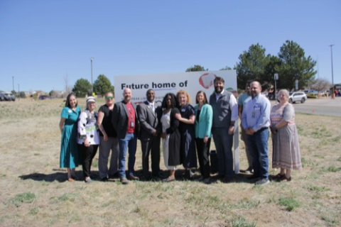 People gathered in a field in front of a sign that says "future home of PPLD" celebrating the purchase of property for Pony Tracks Library 