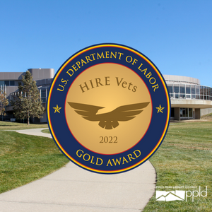 A photo of East Library with the HIRE Vets gold medallion in front. The medallion features an abstract eagle. 