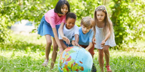 A group of children roll a replica of Earth through the grass